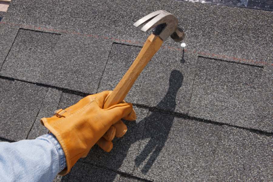 A roofer hammering nail on a shingle roof