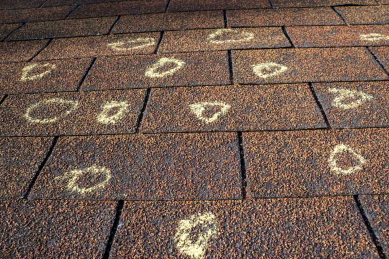 Close-up of roof shingles marked with chalk circles indicating hail damage
