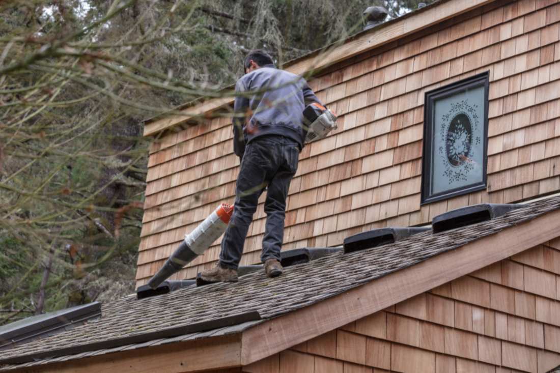 Roof worker blowing debris off cedar shake roof during maintenance in Portland, OR